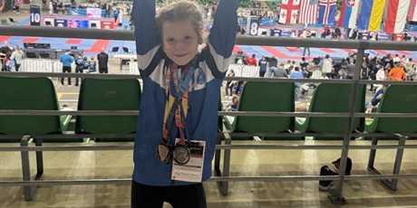 Powiększ grafikę: Dziewczynka z medalami na szyi i pucharami w dłoniach.
