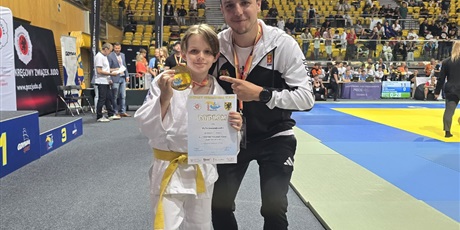 Powiększ grafikę: Zawodniczka trzyma w dłoniach medal i dyplom.