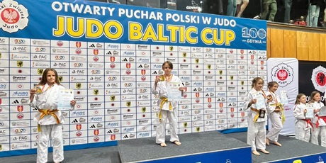Powiększ grafikę: Zawodniczka stojąc na podium, trzyma w dłoniach medal i dyplom.