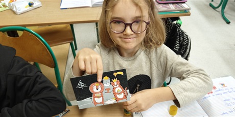 Powiększ grafikę: Dziewczynka pokazuje wybraną przez siebie kartkę pocztową. 