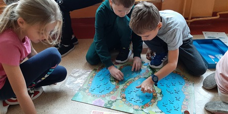 Powiększ grafikę: Chłopcy siedzą na podłodze w sali, grają w gry planszowe.