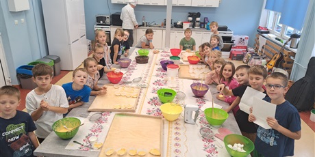 Powiększ grafikę: Grupa dzieci stoi przy stole, gdzie są produkty do zrobienia ciasta dyniowego.