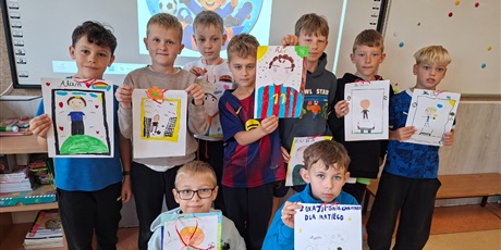Powiększ grafikę: Chłopcy stoją za nimi jest tablica z napisem Dzień Chłopaka. Trzymają w rękach swój portret.