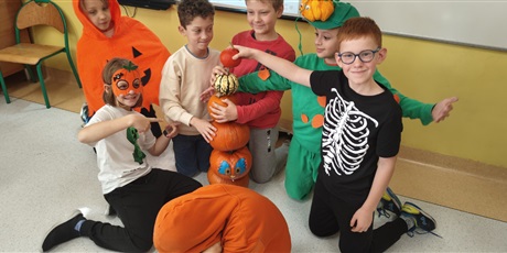 Powiększ grafikę: Dzieci ubrane na pomarańczowo prezentują swoje dynie, kładąc jej jedne na drugim. 