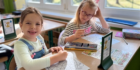Powiększ grafikę: Dwie dziewczynki pracują przy szkolnej ławce podczas zajęć plastycznych.