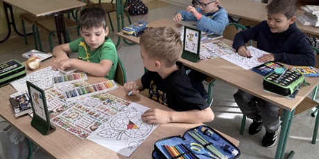 Powiększ grafikę: Czterech chłopców siedzi w podwójnych ławkach w sali lekcyjnej, wykonując prace plastyczne.