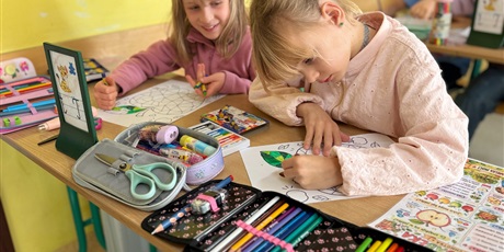 Powiększ grafikę: Bliski kadr na dwie dziewczynki zaangażowane w kolorowanie rysunku.