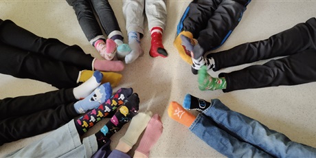 Powiększ grafikę: Uczniowie z klasy 3c na podłodze prezentują w kole swoje kolorowe skarpetki.