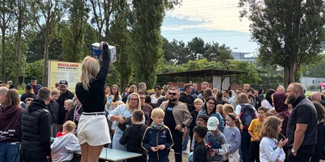 Powiększ grafikę: Pani prowadzi licytację zgromadzonych przedmiotów.
