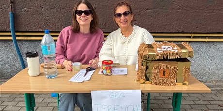 Powiększ grafikę: Organizatorki gry terenowej siedzą przy stoliku.