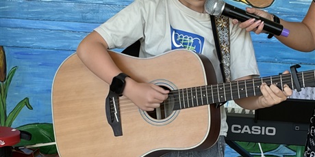Powiększ grafikę: Chłopiec śpiewa i gra na gitarze.
