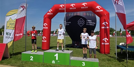 Powiększ grafikę: zawodnicy stoja na 3 stopniach podium