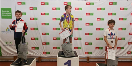 Powiększ grafikę: chłopcy stoją na podium  z medalami na szyi, dyplomem oraz nagrodą rzeczową