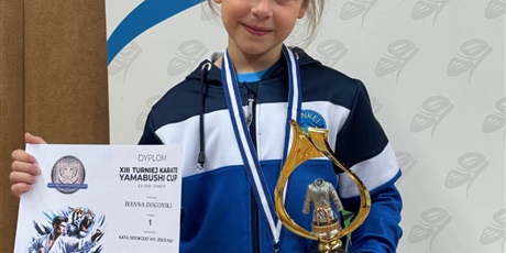Powiększ grafikę: Zawodniczka trzyma dyplom, puchar, na szyi zawieszony złoty medal.