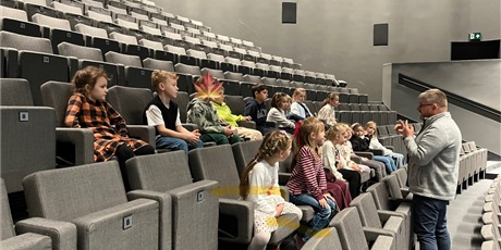 Powiększ grafikę: Dzieci zajęły miejsca na widowni, pan opowiada o teatrze.