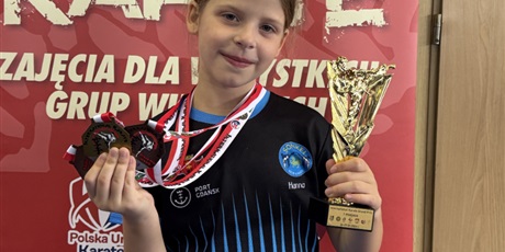 Powiększ grafikę: Dziewczynka w jednej ręce trzyma zdobyte meble, a w drugiej puchar.