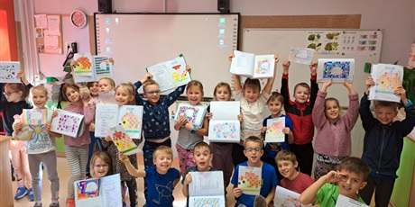 Powiększ grafikę: Grupa dzieci stoi przed tablicą, w rękach trzymają zeszyty z kolorowanką o jeżu. 