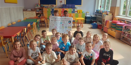 Powiększ grafikę: Dwaj chłopcy stojąca trzymają w ręku plakat  z okazji Międzynarodowego Dnia Kropki. Pozostałe dzieci siedzą przed nimi na podłodze. 
