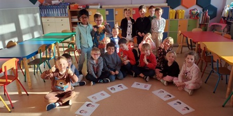 Powiększ grafikę: Niektóre dzieci siedzą na podłodze,   inne stoją. Na ziemi leżą ilustracje przedstawiające dzieci z różnych krajów.