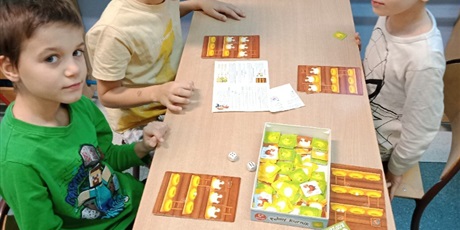 Powiększ grafikę: Trzech chłopców siedzi przy stoliku i grają w grę planszową.