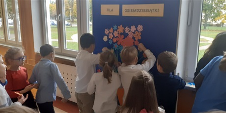 Powiększ grafikę: Dzieci przyczepiają życzenia dla szkoły w kształcie kwiatka, na tablicy, na holu.