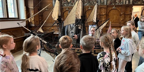 Powiększ grafikę: Dzieci z kl.1b uważnie słucchają opowieści przewodnika w sali Dworu Artusa.