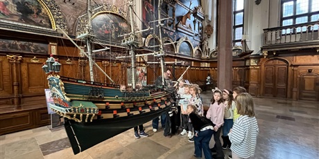 Powiększ grafikę: Dzieci z kl.1b uważnie słucchają opowieści przewodnika w sali Dworu Artusa.