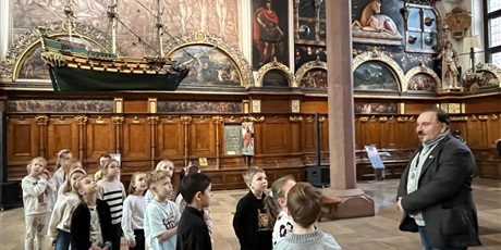 Powiększ grafikę: Dzieci z kl.1b uważnie słucchają opowieści przewodnika w sali Dworu Artusa.