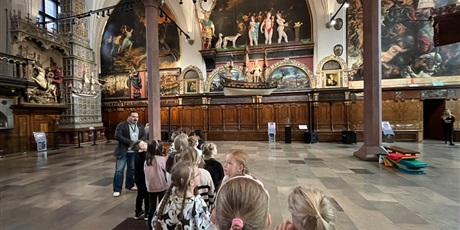 Powiększ grafikę: Dzieci z kl.1b uważnie słucchają opowieści przewodnika w sali Dworu Artusa.