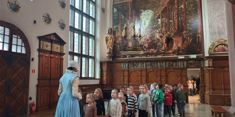 Powiększ grafikę: Dzieci z zerówki słuchają przewodniczki w sali Dworu Artusa.