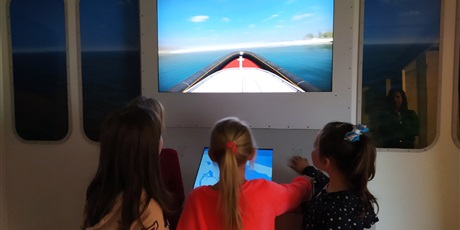Powiększ grafikę: Cztery dziewczynki spoglądają na monitory i sterują łodzią.