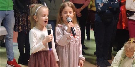 Powiększ grafikę: Po środku dwie dziewczynki z mikrofonami śpiewają piosenkę. W tle tłum ludzi.