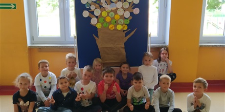 Powiększ grafikę: Grupka dzieci siedzi przed tablicą, na której znajduje się drzewo z kółkami.