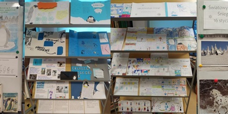 Powiększ grafikę: Po prawej i lewej stronie plakaty z pingwinami i śniegiem, w środkowej części na półkach leżą prace plastyczne i lapbooki o pingwinach