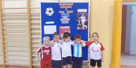 Powiększ grafikę: Drużyna z klasy "0" przed tablicą dotyczącą mistrzostw w piłce nożnej.